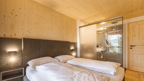 Ein modernes Schlafzimmer mit zwei Betten, Holzboden und einer Duschkabine aus Glas.