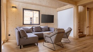 Ein modernes Wohnzimmer mit einem Ecksofa, zwei Sesseln, einem Flachbildfernseher und Holzböden.