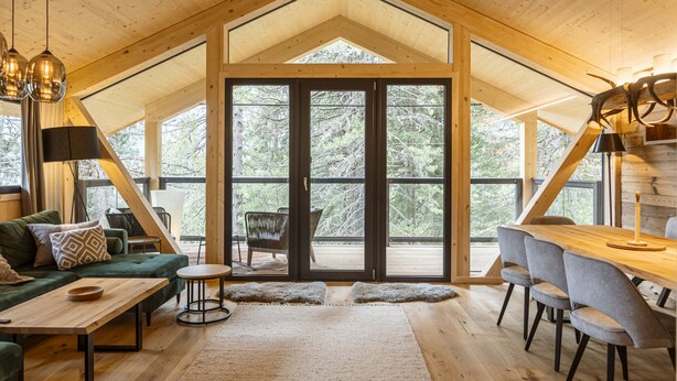 A spacious loft-style room with a high ceiling, large windows, and a cozy seating area with a sofa and chairs.