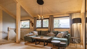 A cozy wooden cabin interior with a green sofa, a small table, and a lamp.