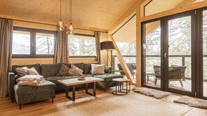 A cozy living room with a green sectional sofa, a wooden coffee table, and a large window with a view of trees.