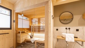 A sauna room with wooden benches and a glass door, a wooden bench with a towel, and a sink with a mirror and towel.