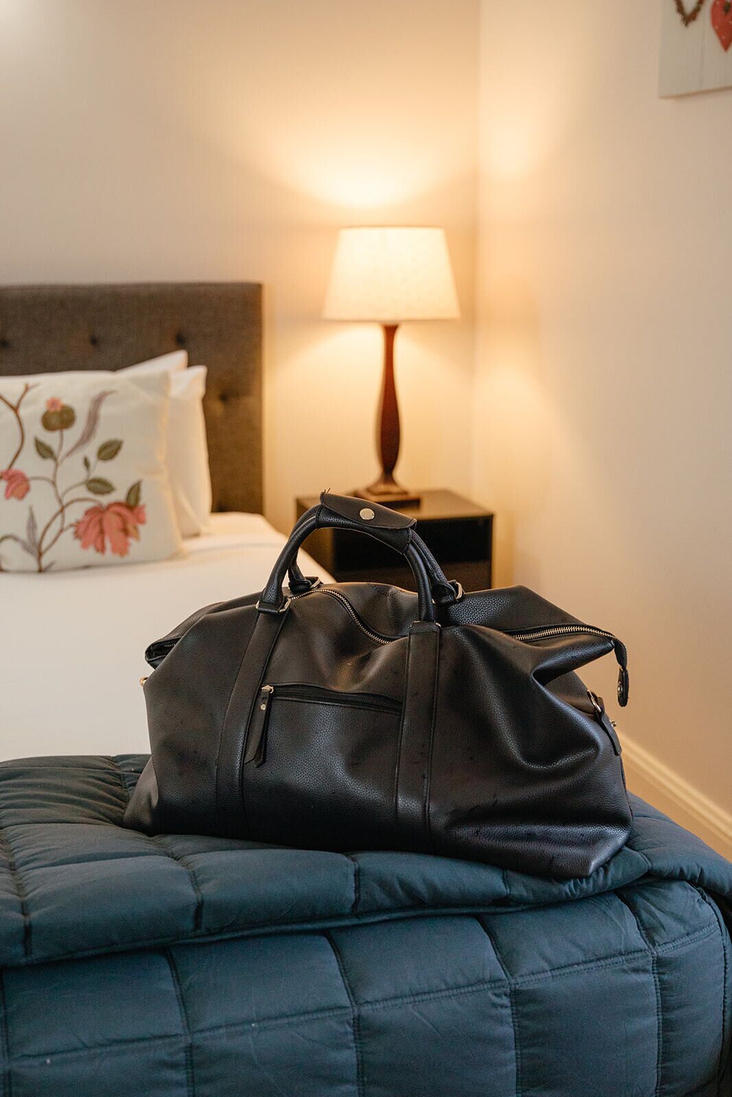 Una cama con un edredón azul oscuro y un bolso de cuero negro encima.