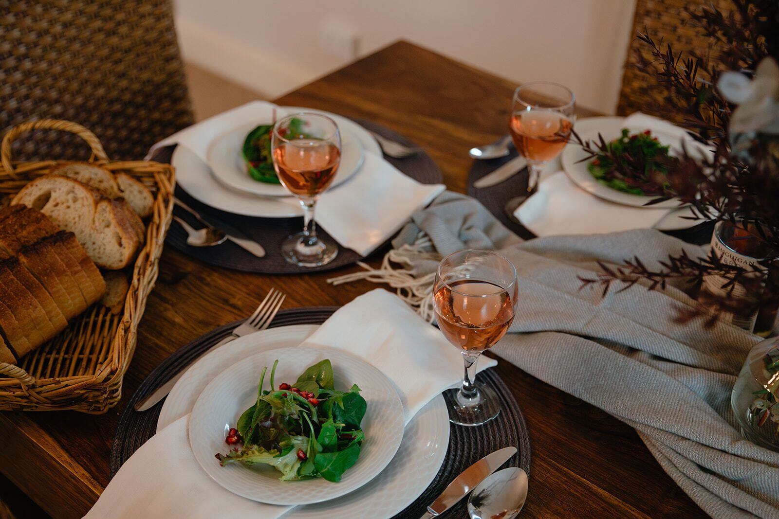 A dining table set with plates of salad, wine glasses, and a basket of bread.