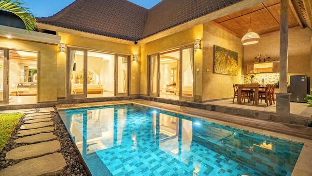 Una piscina con solárium de baldosas, un comedor con mobiliario de madera y una cocina con salpicadero de azulejos.