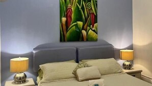 A bedroom with a bed, two bedside tables with lamps, a ceiling fan, and a large abstract painting on the wall. - Posada 1914 (Panama City)