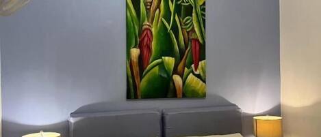 Un dormitorio con una cama, dos mesitas de noche con lámparas, un ventilador de techo y un cuadro abstracto grande en la pared.