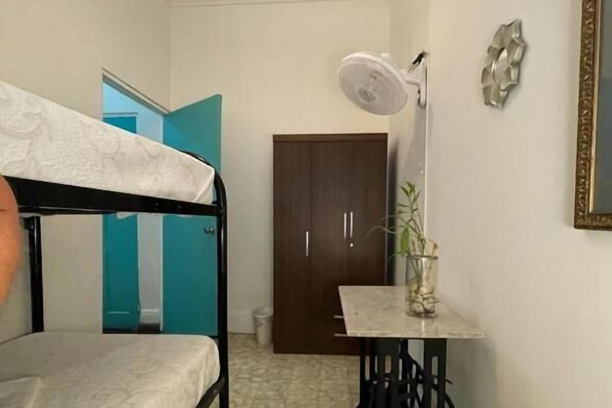 A small, compact room with a bunk bed, a desk with a lamp, and a door leading to another room.