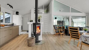 A modern kitchen with a central wood-burning stove, wooden flooring, and a dining area with a table and chairs. - "Annlisa" - 1km from the sea by Interhome (Blokhus)