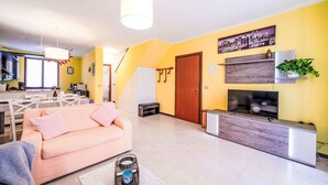 A modern living room with a sofa, a coffee table, a TV, and a kitchen area with a dining table and chairs. - Villaggio 5 Terre by Interhome (Pignone)