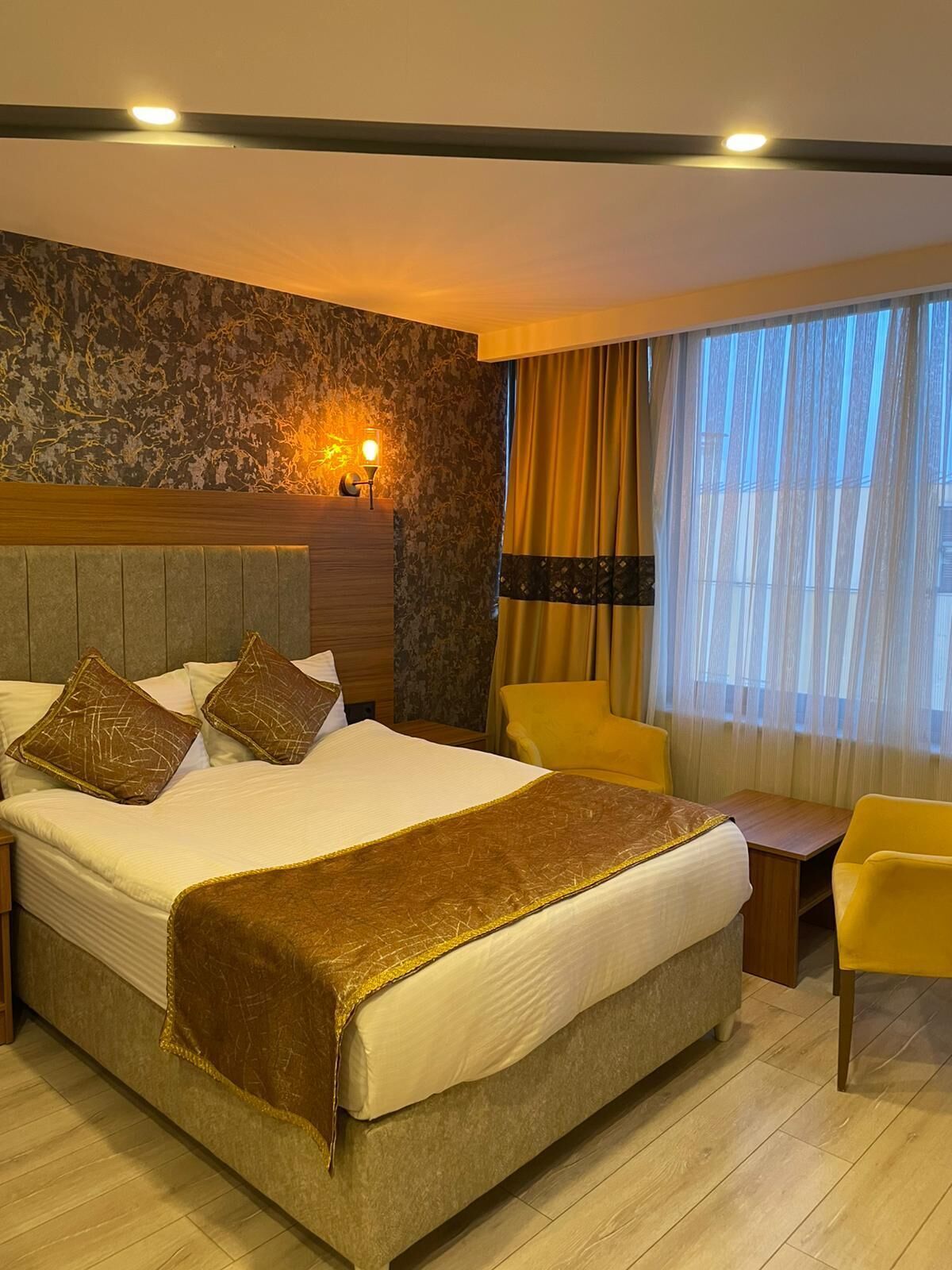 A hotel room with a large bed, a nightstand, a lamp, a chair, and a window with curtains.