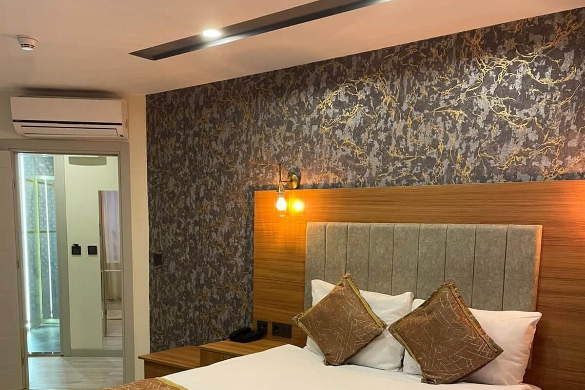Una habitación de hotel moderna con una cama grande, un cabecero de madera y una pared con textura.