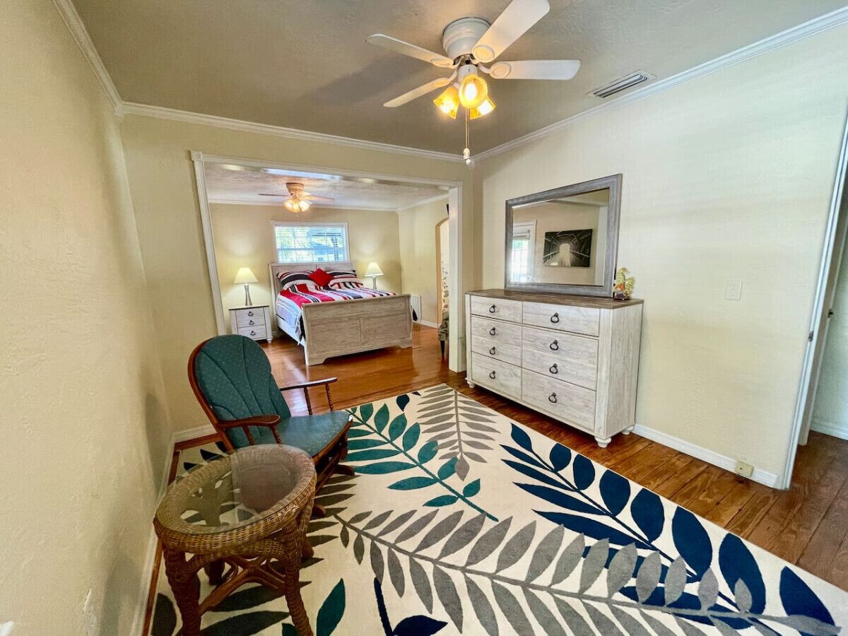 A room with a bed, a dresser, a chair, and a large leaf-patterned rug.