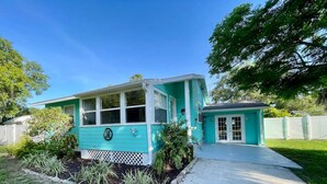 A turquoise house with a front porch, a small attached garage, and a well-maintained lawn.