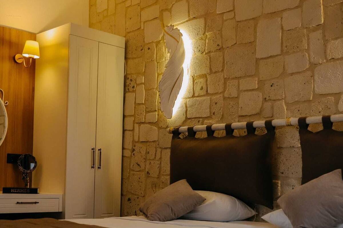 Un dormitorio con pared de piedra, una cama con cabecera, un armario y una lámpara.