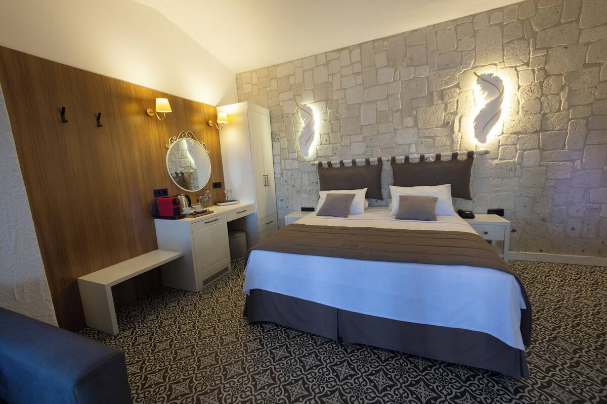 Habitación de hotel con una cama grande, un escritorio de madera, un espejo y una pared de piedra.