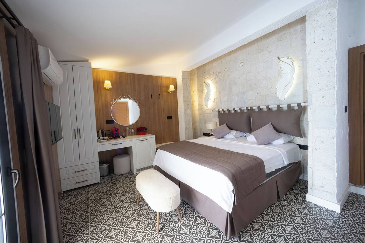 Un dormitorio con cama, mesita de noche, espejo, armario e iluminación de pared.
