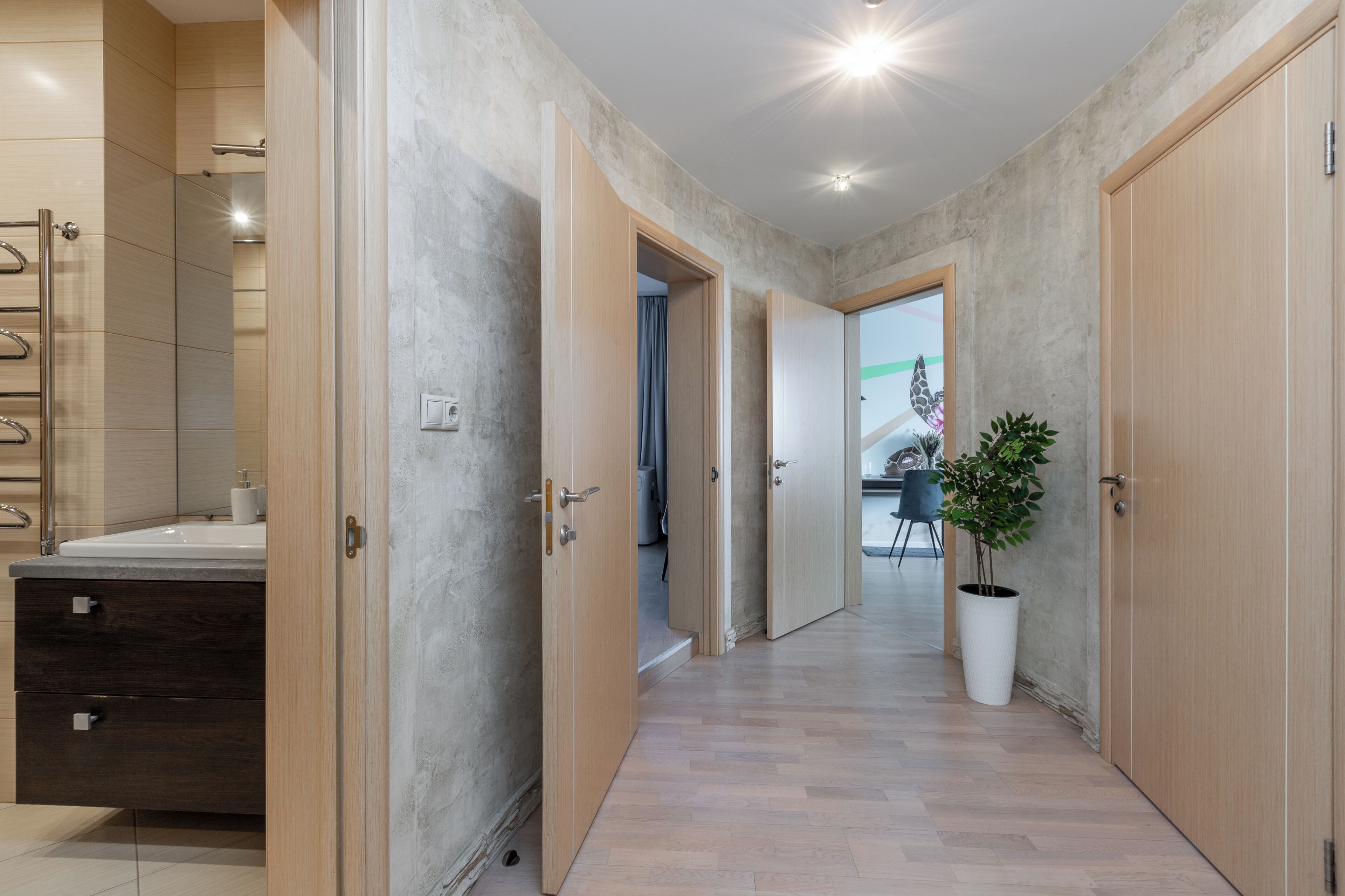 Un pasillo con un baño a la izquierda, puertas de madera y una planta en maceta.