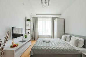 Un dormitorio moderno con una cama grande, un televisor sobre un mueble blanco, un armario y una ventana con cortinas.