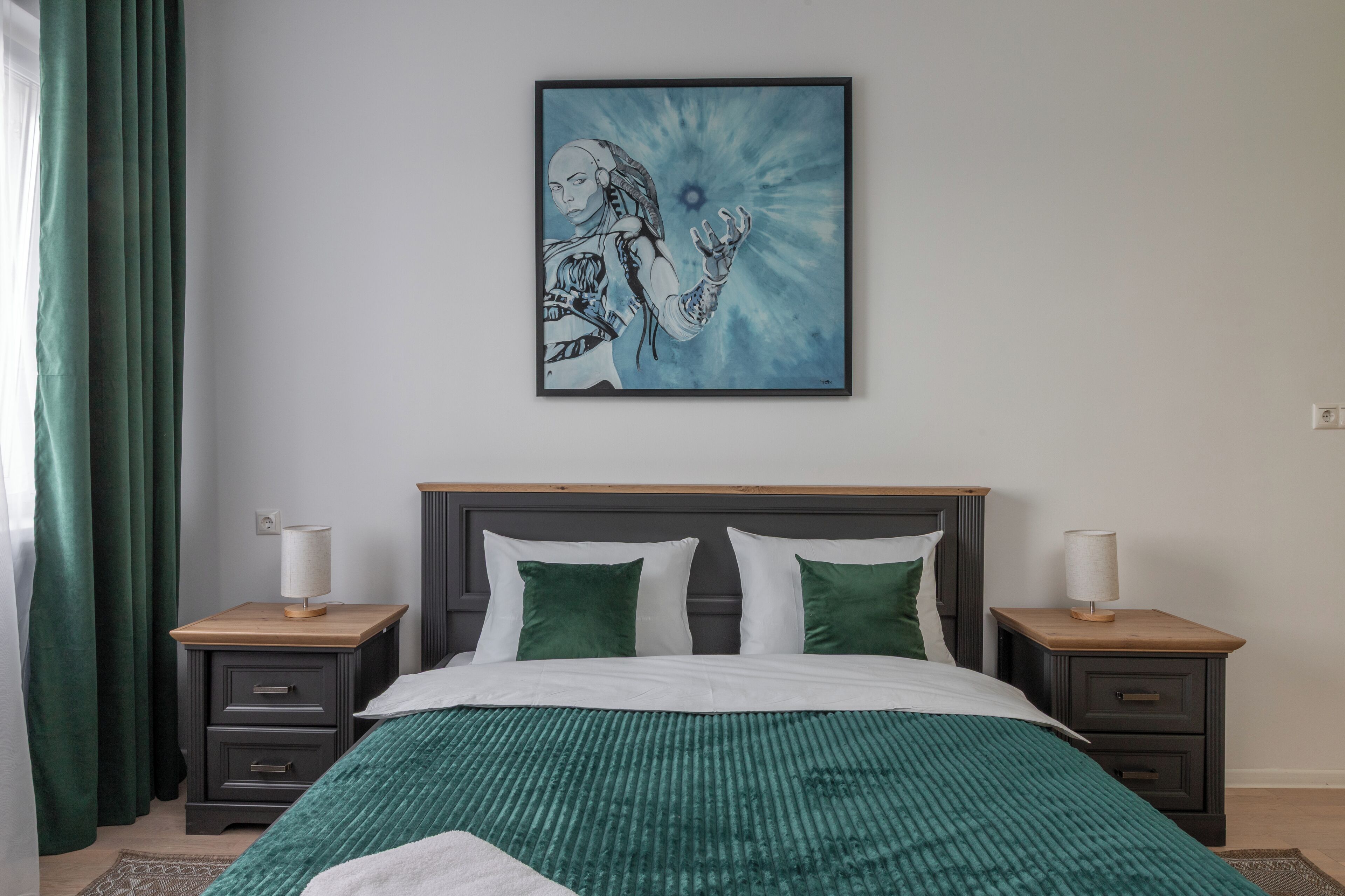 Ein Schlafzimmer mit einem Bett, zwei Nachttischen, einem Wandkunstwerk und einem grünen Vorhang.