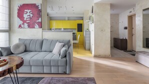 Uma sala de estar moderna com um sofá cinzento, uma mesa de centro de madeira e um quadro abstrato grande na parede.