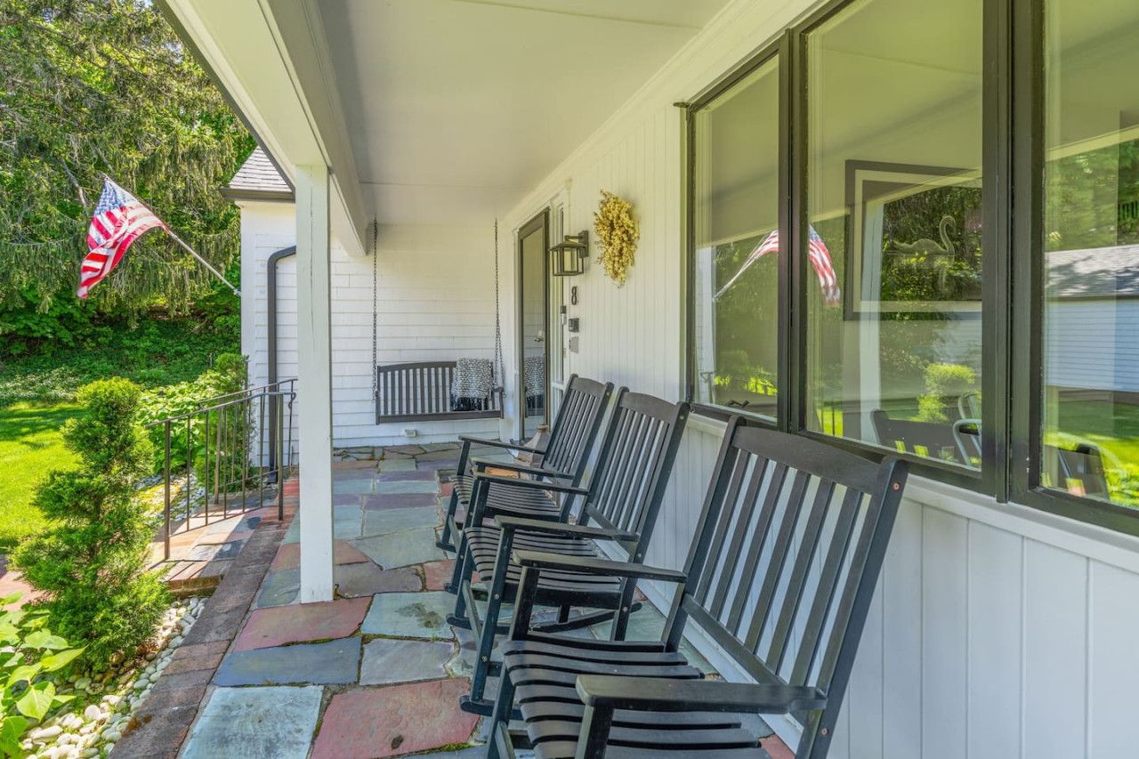 A covered porch with a row of black chairs, a small table, and a flag.