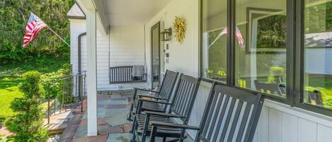 A covered porch with a row of black chairs, a small table, and a flag.
