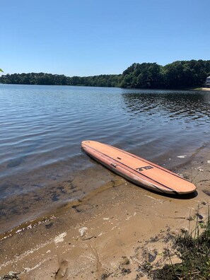 A wooden paddleboard on a sandy shore with a lake and forest in the background. - Stunning Waterfront Home with Hot Tub, Deck, Fire Pits, Office & More (Dennis)