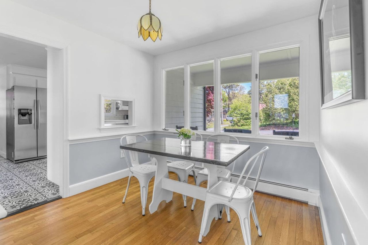 A modern kitchen with white cabinetry, a glass-top dining table, and a view of the outdoors through large windows.