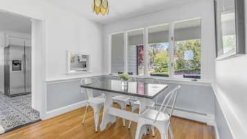 A modern kitchen with white cabinetry, a glass-top dining table, and a view of the outdoors through large windows.