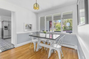 Una cocina moderna con muebles blancos, una mesa de comedor con cubierta de vidrio y vistas al exterior a través de amplios ventanales.