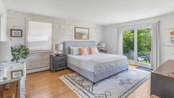 A bedroom with a bed, bedside tables, a nightstand, a window, and a view of greenery.