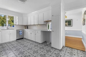 A kitchen with white cabinets, a tiled floor, and a window providing natural light. - Stunning Waterfront Home with Hot Tub, Deck, Fire Pits, Office & More (Dennis)
