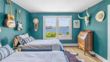 A bedroom with two beds, a dresser, a guitar, a clock, and a large window with a view of the water.
