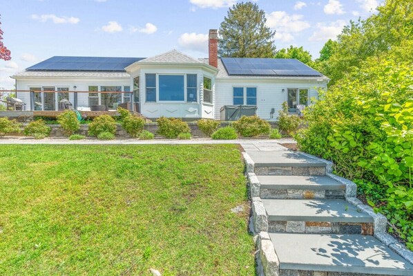 A two-story house with solar panels on the roof, a well-maintained lawn, and a stone staircase leading to the front door.