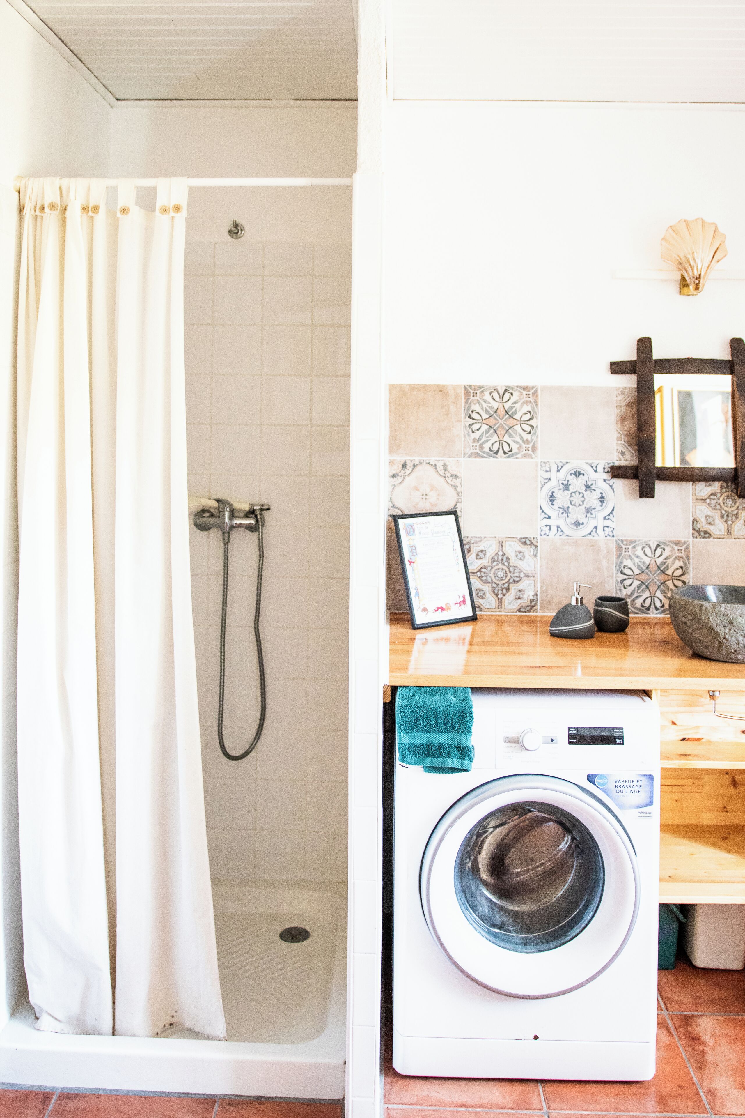 A bathroom with a shower, a washing machine, and a tiled backsplash.