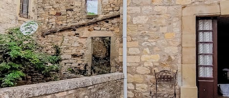 A stone building with a rustic exterior, a metal chair, and a small garden area.