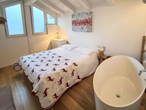 A bedroom with a bed, a large bathtub, a nightstand, and a wall-mounted painting. - Ai Grecc by Interhome (Lago di Ledro)