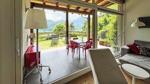 Una camera moderna con un'ampia porta scorrevole in vetro che dà su un patio esterno con tavolo e sedie, un divano e una lampada.