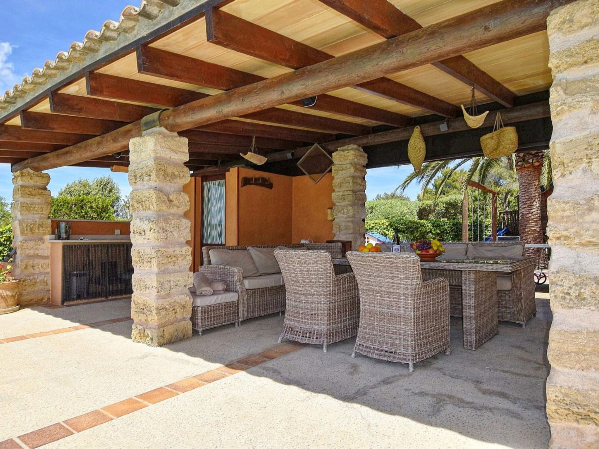 Une terrasse extérieure aménagée avec des meubles en osier, des piliers en pierre et un espace abrité doté d’un plafond en bois.
