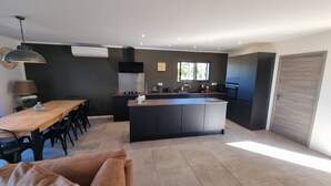 A modern kitchen with a central island, dark cabinetry, and a dining area with a wooden table and chairs. - Villa de Standing Avec T2 Indépendant vue Panoramique (Sotta)