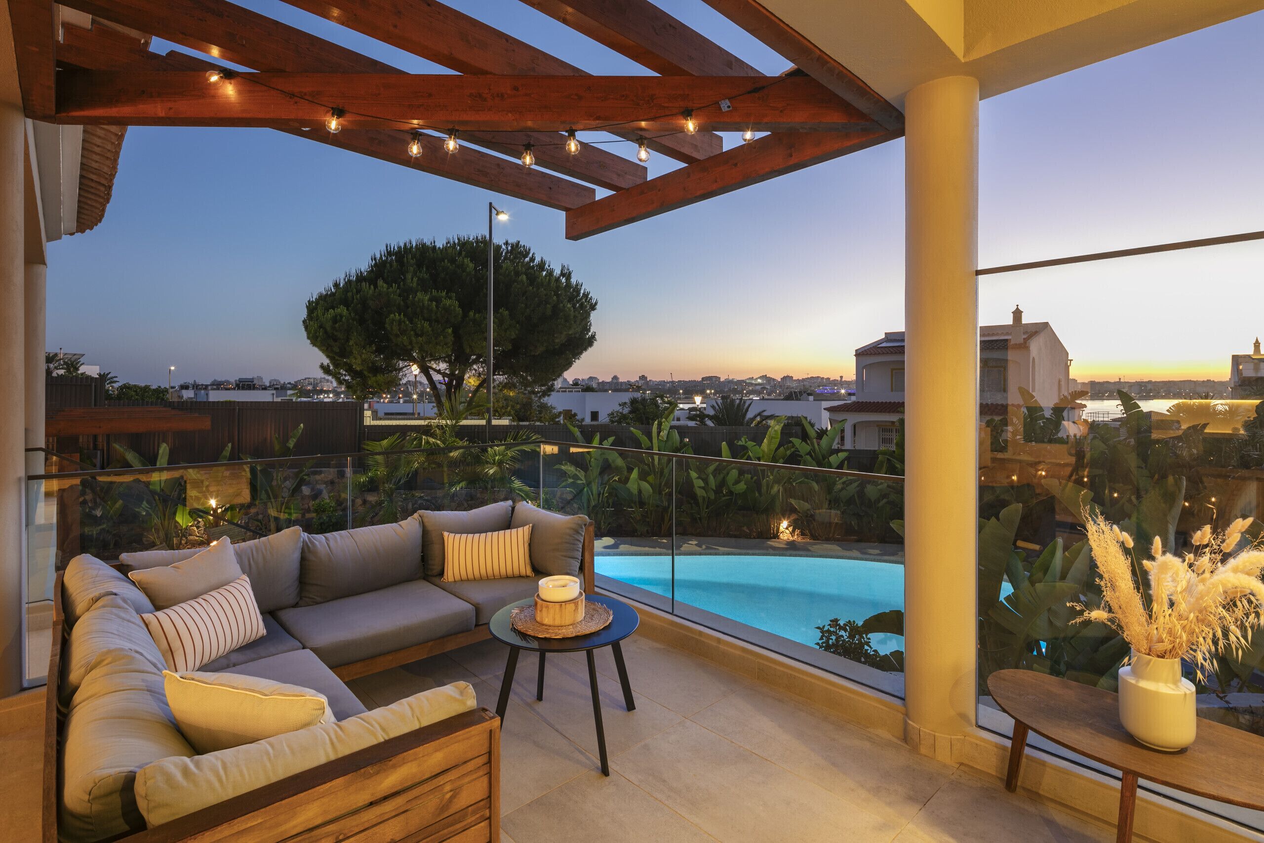 A modern outdoor seating area with a pool view, featuring a sofa, a small table, and a potted plant.