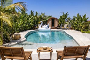 Una piscina con galleggianti a forma di cigno, circondata da palme e lettini da spiaggia.