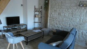 Una sala de estar con un televisor, una mesa de centro de madera, un sofá azul y una silla estampada.