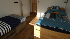 Una habitación pequeña y bien iluminada, con dos camas, piso de madera y una lámpara fijada a la pared.