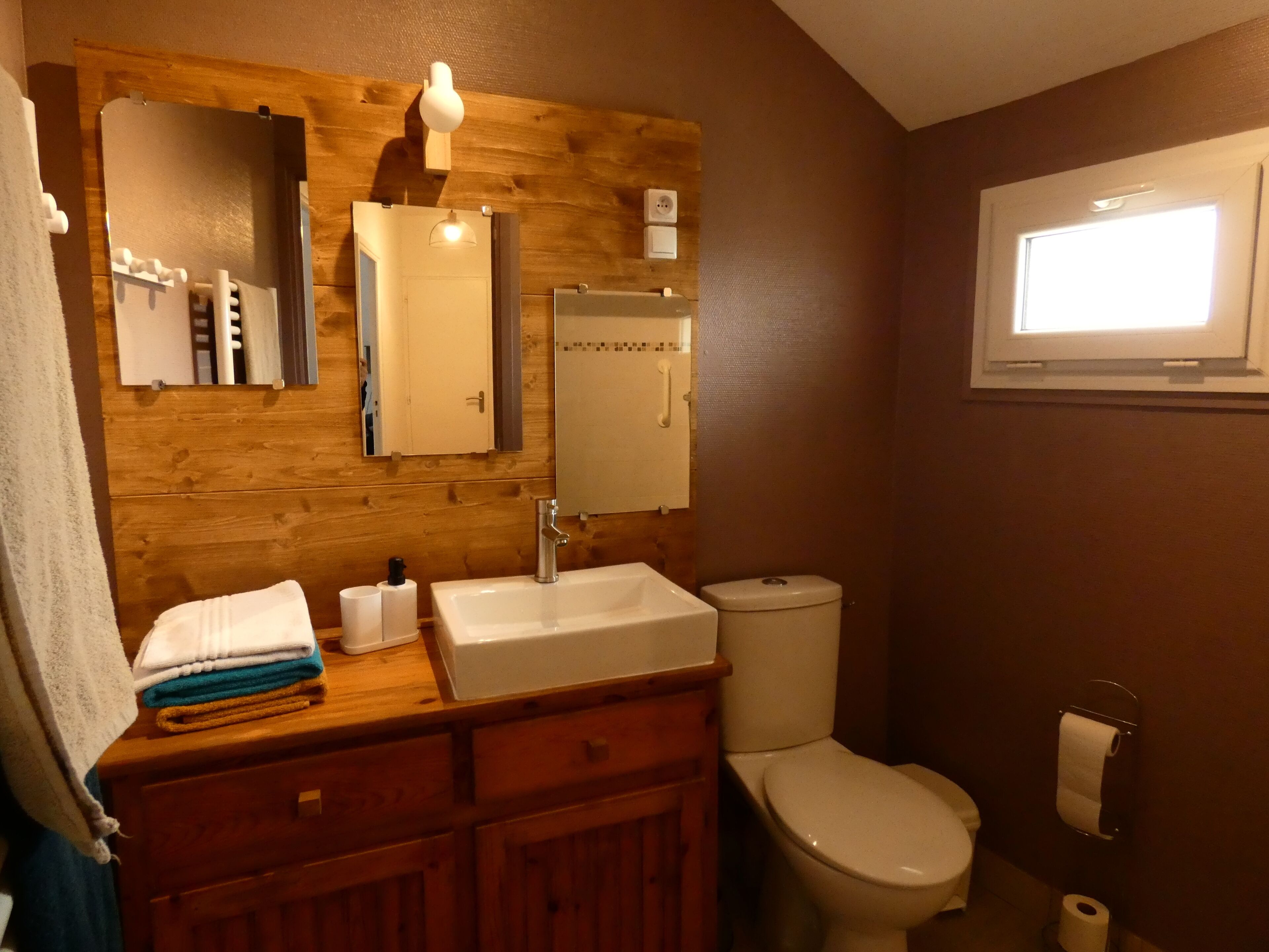 A bathroom with a wooden vanity, a sink, a mirror, a toilet, and a window.