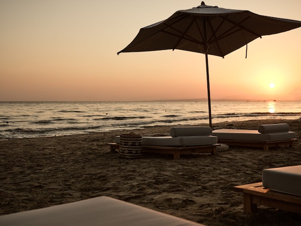 A beach with lounge chairs and an umbrella, overlooking the ocean at sunset.