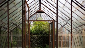 A greenhouse structure with a glass roof and walls, a brick pathway leading through the center, and a green landscape visible outside. - La Petite For t Antique Countryside Greenhouse (Asse)