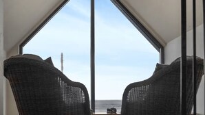 A room with a large window offering a view of the sea. There are two wicker chairs positioned in front of the window.