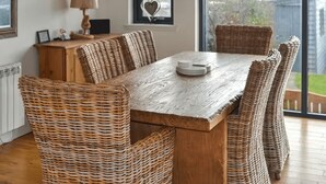 A dining area with a wooden table and wicker chairs, a lamp, and a view of the outdoors.